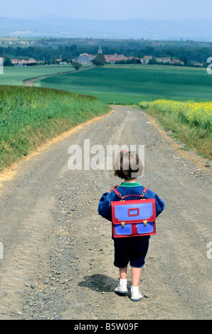 Little girl walking along a country road going to the village school in the countryside Stock Photo