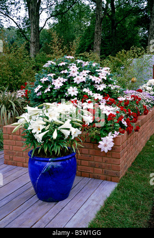 A colourful raised flower bed with container of Lillies Stock Photo