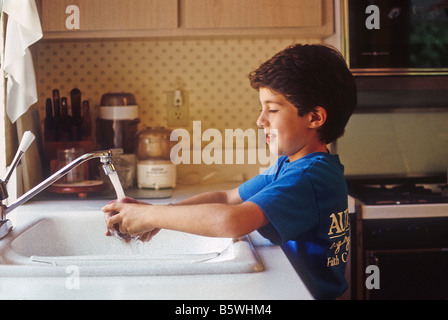 Young boy washes hands in kitchen sink. Stock Photo