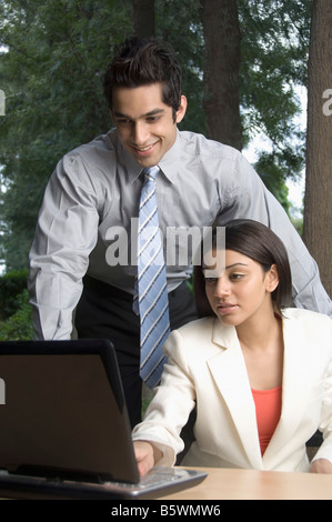 Businesswoman working on a laptop with a businessman standing beside her Stock Photo