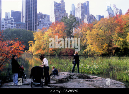 Central Park, New York autumn foliage. People on a rock overlooking the Pond in the Hallett Nature Sanctuary. View of Central Park South skyline. USA Stock Photo