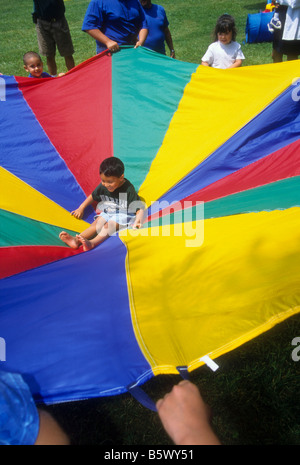 Family bounce child on large colorful parachute at family picnic Stock Photo