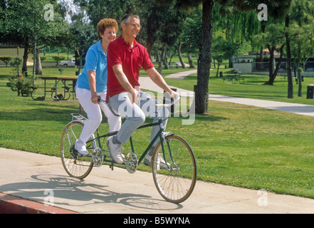 Senior couple ride tandem bicycle built for two in park. Stock Photo