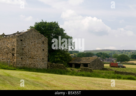 A view across fields - a derelict barn in the foreground and a tractor working alongside a forage harvester, in the background Stock Photo