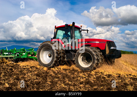 A tractor pulling a disk ripper tills existing field stubble to begin the ground preparation to prepare a seedbed for potatoes Stock Photo