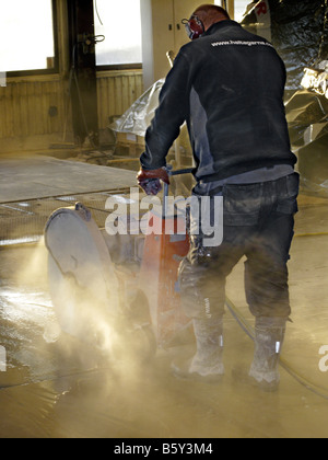 Man operates concrete cutting saw indoors making slabs for removal repair of the floor Stock Photo