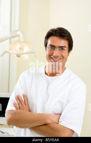 dentist with arms folded smiling and standing in his office Stock Photo