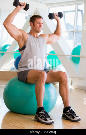 Man Using Hand Weights On Swiss Ball At Gym Stock Photo