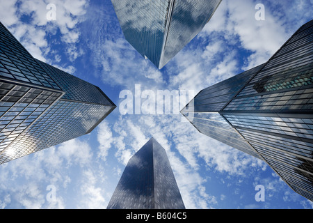 Looking up through four tall glass skyscrapers in Manhattan to a could filled sky. Stock Photo