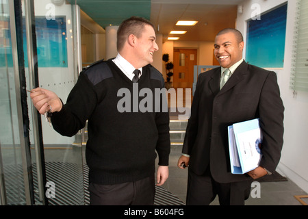 A SECURITY GUARD ON PATROL UNLOCKS THE DOOR OF A BUSINESS PREMISES TO ALLOW A LATE WORKING EMPLOYEE TO LEAVE UK Stock Photo