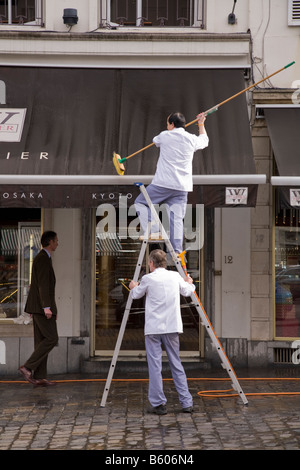 Shop workers clean the awning of a shop in Place du Grand Sablon, Bruxelles. Belgium. (44) Stock Photo