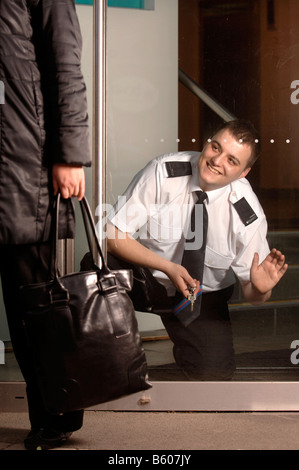 A SECURITY GUARD ON PATROL LOCKS THE DOOR OF A BUSINESS PREMISES UK Stock Photo