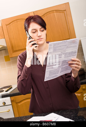 Young woman at home paying or querying a bill using her mobile phone listening and concentrating MR PR Stock Photo
