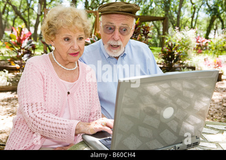 Senior couple using their laptop computer in lovely outdoor setting He s shocked by what he sees online Stock Photo
