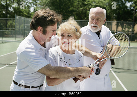 Senior lady taking tennis lessons from a handsome pro while her husband looks on jealously Stock Photo