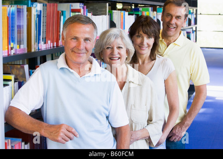 Four people in library standing by bookshelves Stock Photo