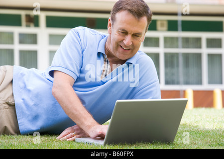 Man lying on lawn of school using laptop Stock Photo