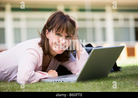 Woman lying on lawn of school with laptop Stock Photo