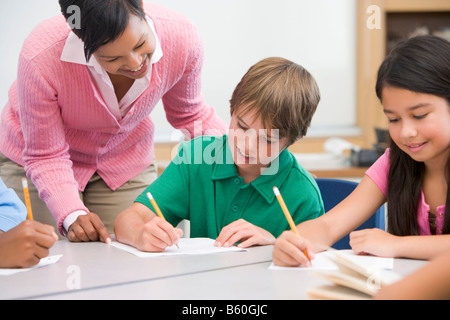 Students in class writing with teacher helping Stock Photo