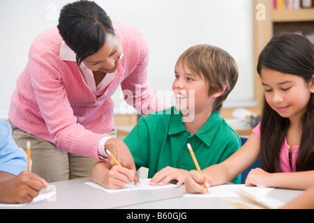 Students in class writing with teacher helping Stock Photo