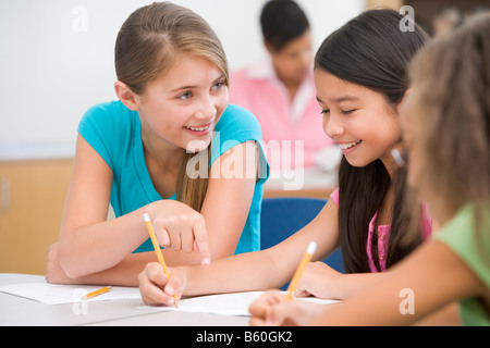Students in class writing and talking with teacher in background (selective focus) Stock Photo