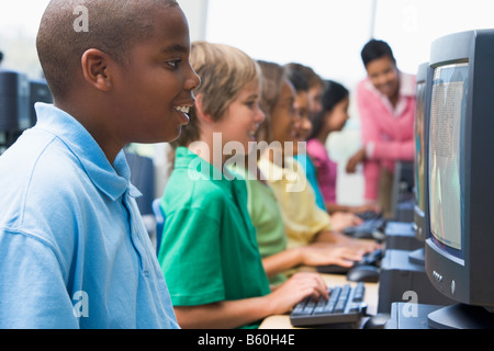 Six children at computer terminals with teacher in background (depth of field/high key) Stock Photo