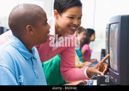Teacher helping student at computer terminal with students in background (depth of field/high key) Stock Photo
