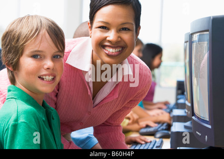 Teacher helping student at computer terminal with students in background (depth of field/high key) Stock Photo