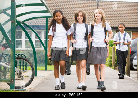 Three students leaving school with other students in background Stock Photo