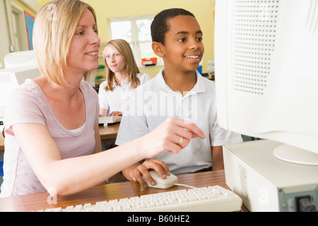 Student and teacher at computer terminal with student in background Stock Photo
