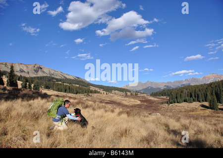 a man backpacks through an alpine meadow with his dog high up in the san juan mountains near telluride colorado Stock Photo