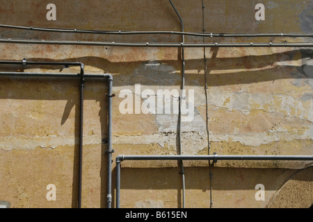 electricity power wiring circuit pipes tubes on side of property wall in sun Stock Photo