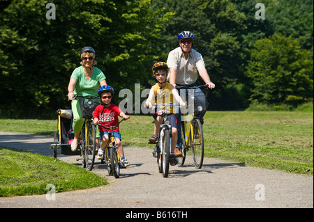 Family with 2 children riding bicycles through a park, wearing helmets Stock Photo