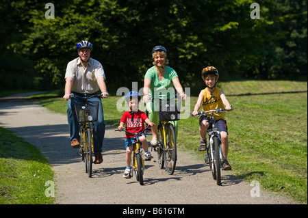 Family with 2 children riding bicycles through a park, wearing helmets Stock Photo