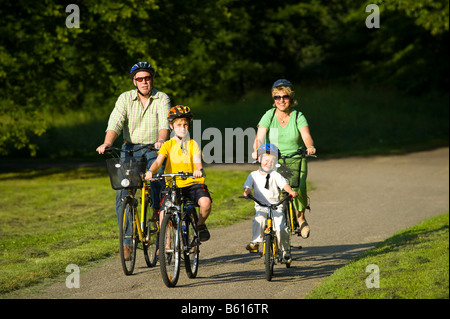 Family with 2 children riding bicycles through a park, wearing helmets Stock Photo