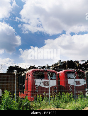 Electric locomotives in a scrapyard, behind them piled-up old metal parts Stock Photo