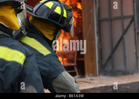 Two fire fighters surrounded by smoke while putting out a fire with a hose line in a container Stock Photo