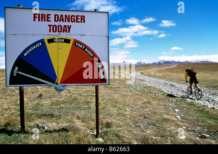 Mountainbiker riding past a Fire Danger sign, Lindis Pass, South Island, New Zealand Stock Photo