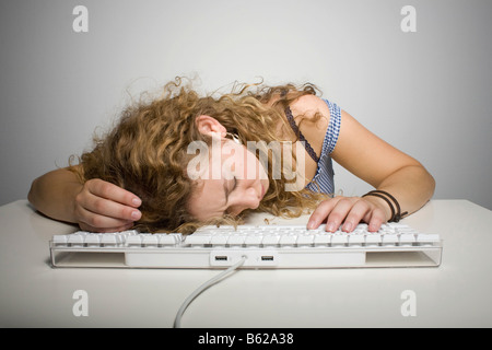 Young woman with long hair resting her head on a computer keyboard on a table Stock Photo