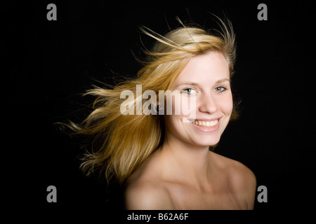 Young blond woman with long blowing hair in front of black Stock Photo