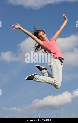 Young dark-haired woman jumping in front of blue sky Stock Photo