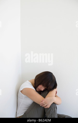 Sad young woman sitting in a corner Stock Photo