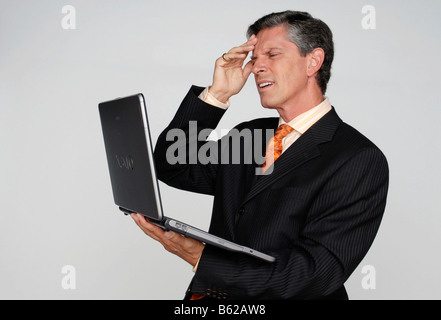 Man slapping his forehead, holding a laptop in the other hand Stock Photo