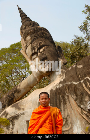 Buddhist monk wearing an orange robe in front of a Reclining Buddha statue, Buddha Park, Suan Xieng Khuan, near Vientiane, Laos Stock Photo