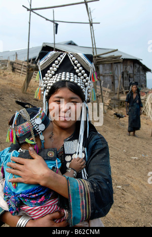 Mother of the Akha Meuo tribe dressed in traditional costume, holding her baby in her arms, in the back the grandmother, Ban Ch Stock Photo