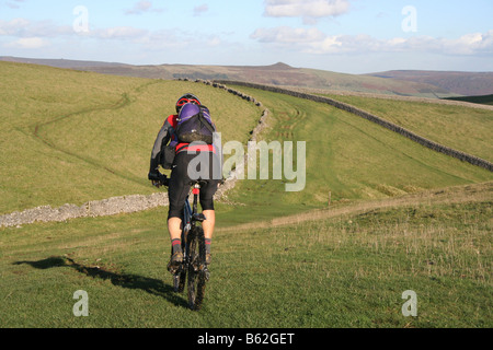 Solo mountain biker crossing open meadow with stone walls above Cave Dale in the Peak District, with Win Hill on horizon Stock Photo