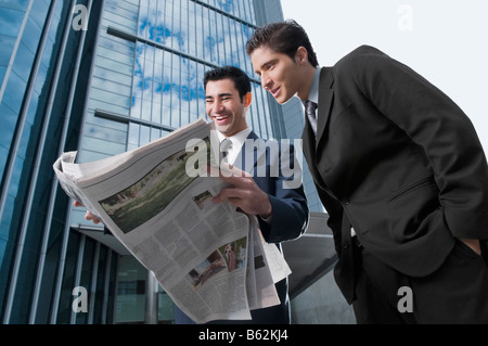 Two businessmen reading a newspaper and smiling Stock Photo