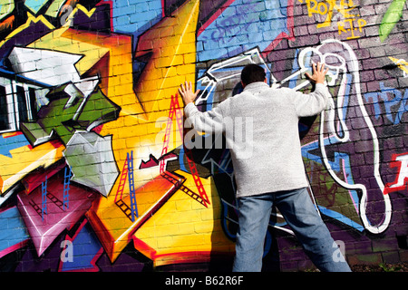 man standing against and facing a wall which has graffiti art on it graffiti spray paint brick wall art painting Stock Photo