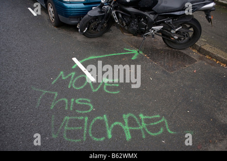A request to move this vehicle has been mis-spelled by sprayed aerosol on the road's surface in a residential London street Stock Photo