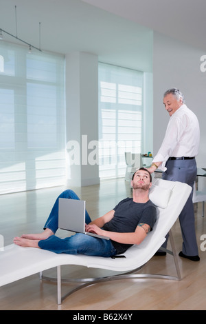 Young man using a laptop with his grandfather standing behind him Stock Photo